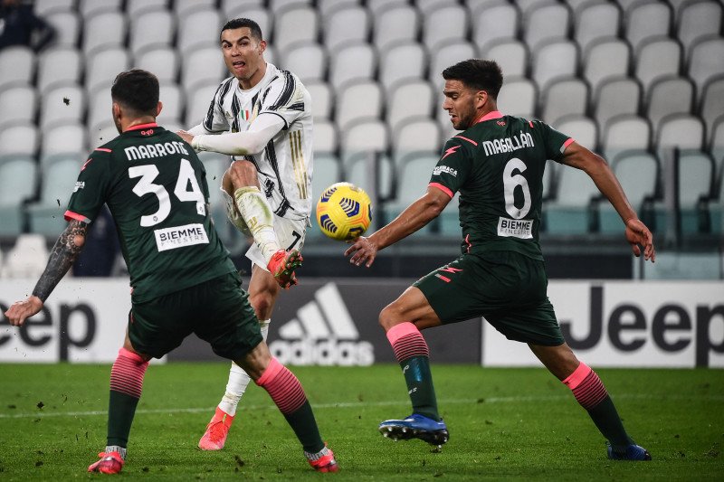 Penyerang Juventus Cristiano Ronaldo melepas tembakan diantara dua pemain Crotone Luca Marrone (kiri) dan Lisandro Magallan saat pertandingan Liga Italia di Turin, Italia, Senin (22/2/2021) (Photo by Marco BERTORELLO / AFP) (AFP/MARCO BERTORELLO)
