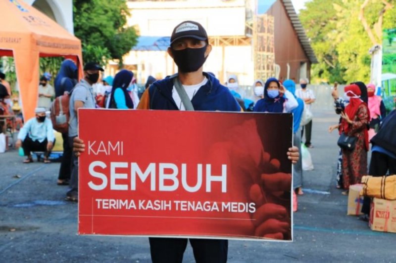 SEMBUH: Seorang warga yang dinyatakan sembuh dari COVID-19 membawa spanduk bertuliskan ucapan terima kasih kepada tenaga medis saat dipulangkan dari tempat karantina di Asrama Haji Surabaya pekan lalu. | PEMKOT SURABAYA