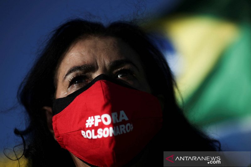 Seorang pengunjuk rasa memakai masker pelindung bertuliskan "Out Bolsonaro" berpartisipasi dalam sebuah protes terhadap Presiden Brazil Jair Bolsonaro dan cara ia menangani penyebaran penyakit virus korona (COVID-19) di Brasilia, Brazil, Minggu (24/1/2021