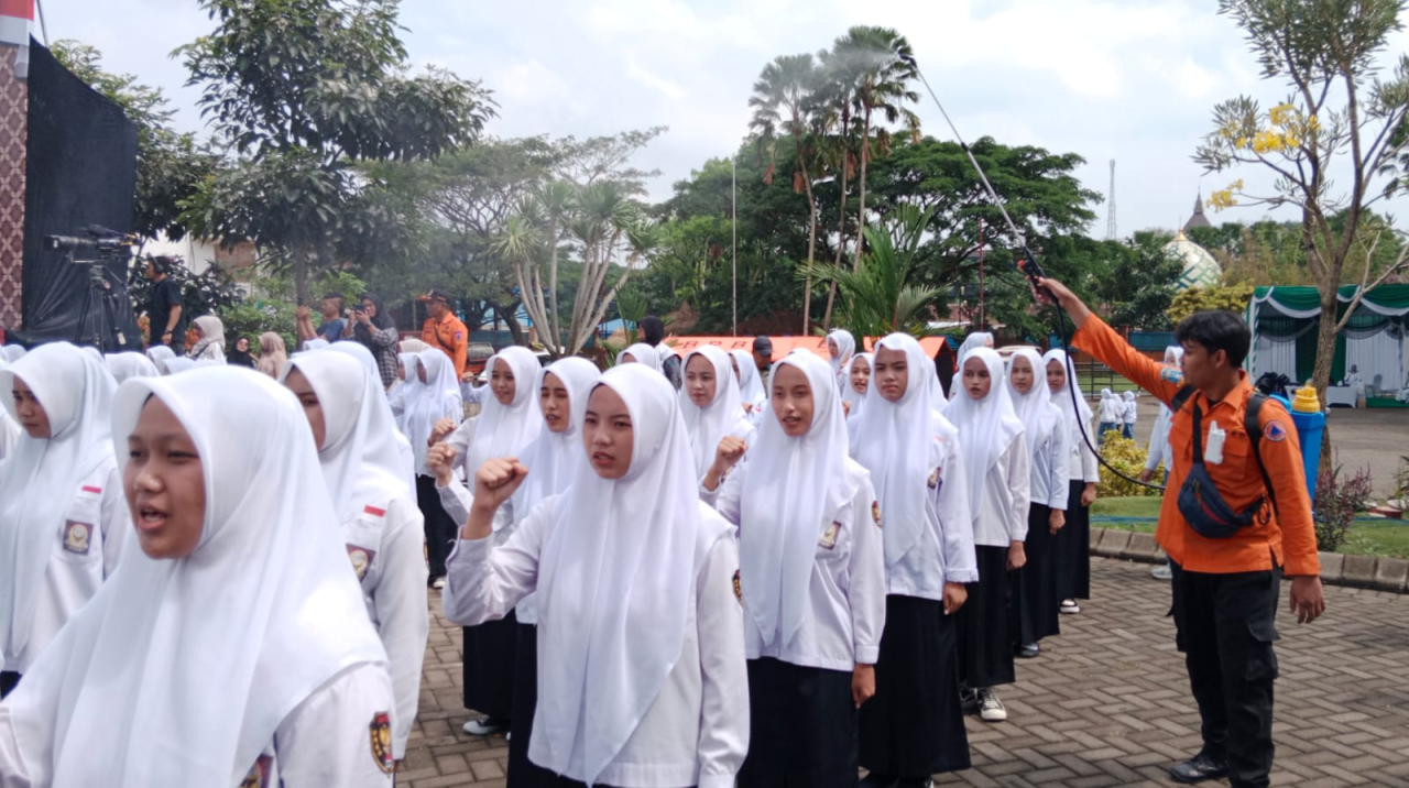 Untuk mengurangi panas, seorang petugas menyemprotkan air (embun buatan) di atas peserta apel peringangatan Hari Santri 2025 di Ponpes An Nur, Bululawang, Malang, Rabu (22/10)