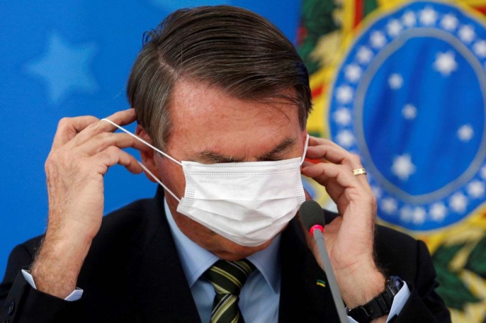 Presiden Brasil Jair Bolsonaro memperbaiki maskernya saat memberikan keterangan media mengenai langkah pemerintah untuk mengendalikan penyebaran virus COVID-19 di Brasilia, Brasil, Rabu (18/3/2020). (REUTERS/ADRIANO MACHADO)