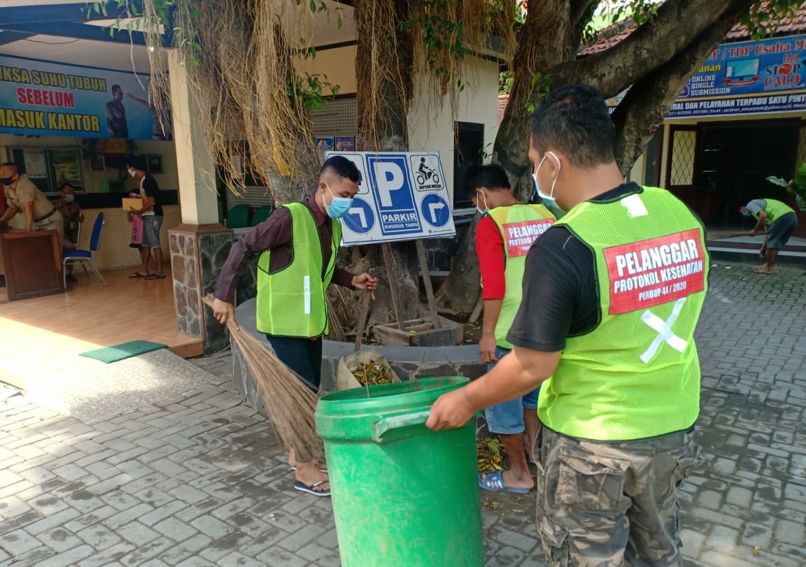 Pelanggar penggunaan masker sedang menyapu di Kantor Kecamatan Krian. (FOTO: HMP/lis)