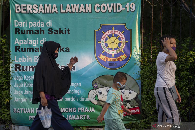 Sejumlah warga dengan mengenakan masker berjalan dengan latar belakang spanduk peringatan bahaya COVID-19 di Sunter, Jakarta, Sabtu (22/8/2020). Data Satuan Tugas Penanganan COVID-19 per hari Sabtu (22/8) . dok.ant