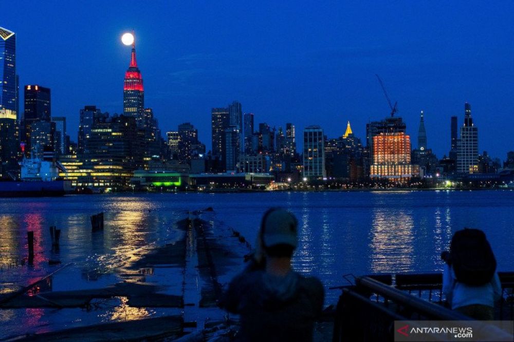 DI BALIK KEINDAHAN NEW YORK: Bulan purnama (Supermoon) terlihat di belakang gedung Empire State menyala IDmerah, bersamaan dengan mewabahnya virus corona (COVID-19) yang sedang melanda, di wilayah Manhattan, New York City, dilihat dari Hoboken, New Jersey