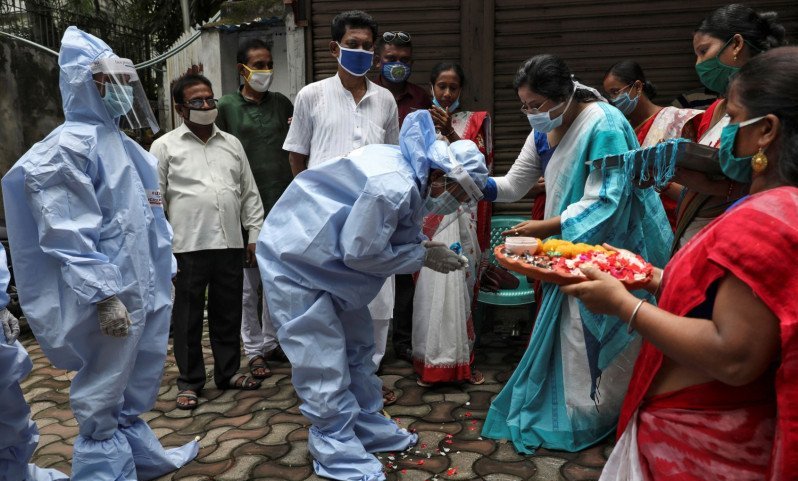 Seorang perempuan mengikatkan Rakhi, sebuah benang suci tradisional India, pada pergelangan tangan pekerja pemerintah kota yang memakai alat pelindung diri (APD) untuk merayakan festival Hindu Raksha Bandha, dimana seorang saudara perempuan mengikat satu 