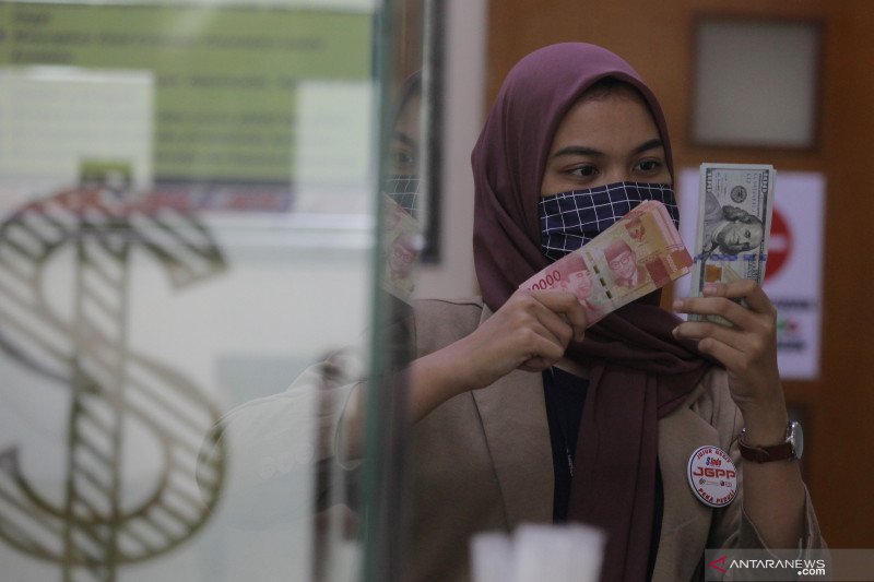  Karyawati menunjukkan mata uang rupiah dan dolar AS di salah satu gerai penukaran mata uang asing di Jakarta, Minggu (7/6/2020). ANTARA FOTO/Reno Esnir/aww. (ANTARA/RENO ESNIR) 