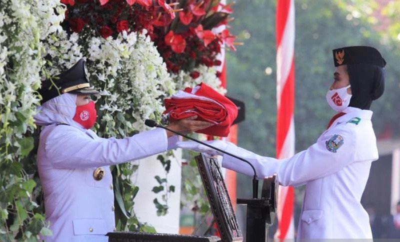 Petugas Paskibraka Findar Amelia Hariami (kanan) saat menerima bendera Merah Putih dari Gubernur Jawa Timur Khofifah Indar Parawansa (kiri) di sela upacara memperingati HUT Ke-75 RI di halaman Gedung Negara Grahadi di Surabaya, Senin (17/08/2020) pagi. (A