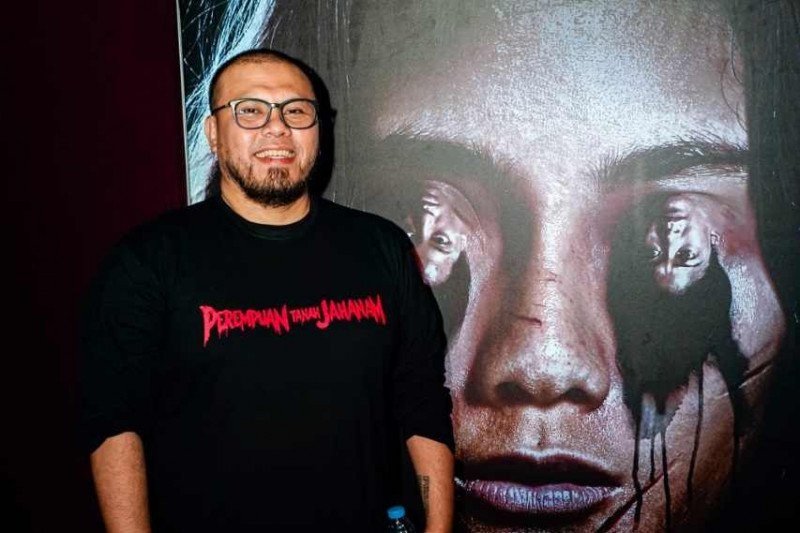 Sutradara Joko Anwar berpose di depan poster film "Perempuan Tanah Jahanam" di Jakarta, Senin (16/9/2019). (Antaranews/HO/ist)

