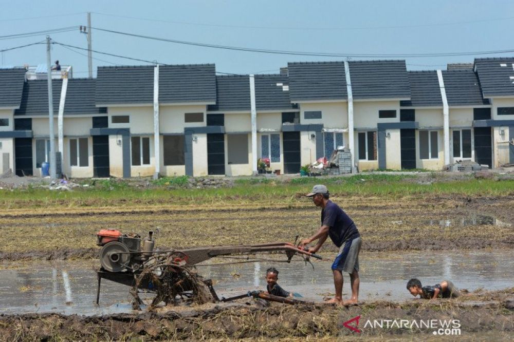 Buruh tani membajak sawah menggunakan traktor dengan latar belakang perumahan di areal persawahan Desa Segodorejo, Kecamatan Sumobito, Jombang, Jawa Timur, Kamis (16/4/2020). (FOTO: HMP/SYAIFUL ARIF) 